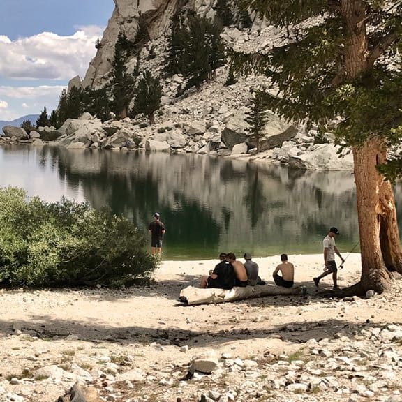 A group of people are sitting on a log near a lake