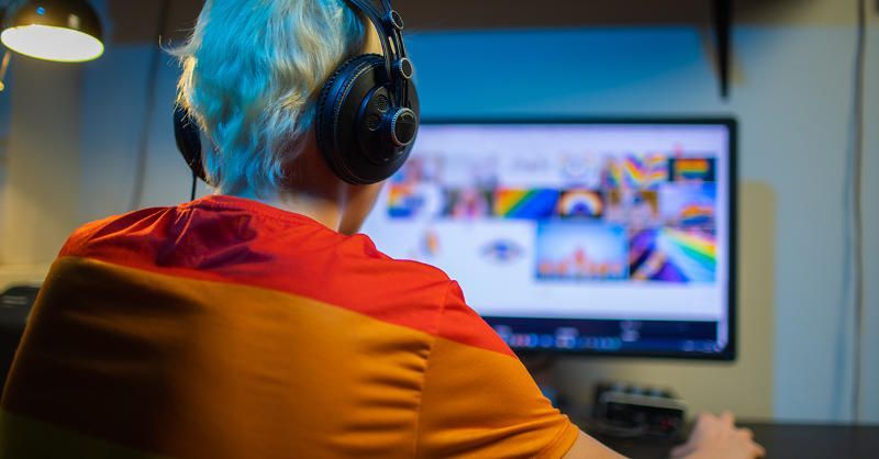 A man with blue hair is wearing headphones and looking at a computer screen.