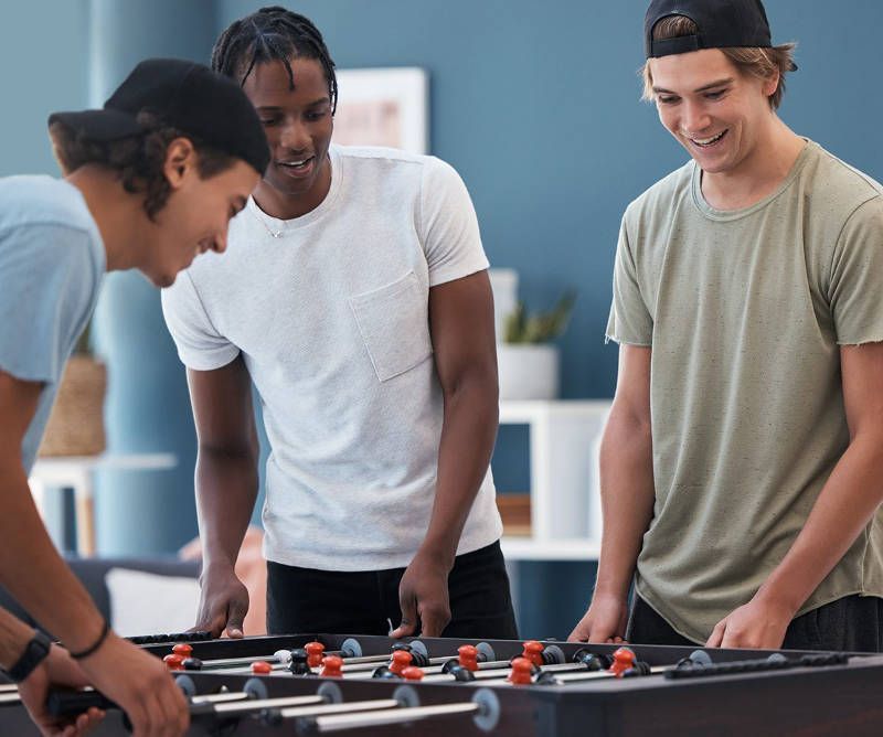 Three young men are playing a game of foosball in a living room.