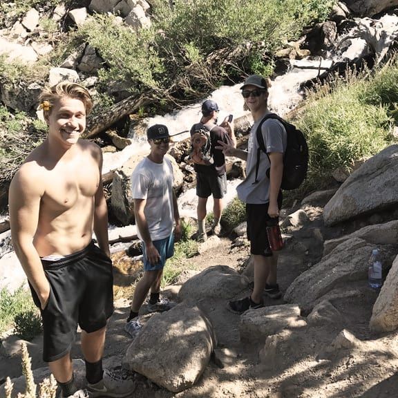 A group of young men are standing on a rocky trail near a waterfall