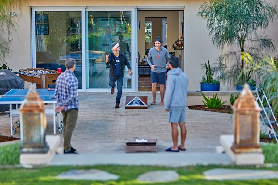 A group of men are playing cornhole on a patio in front of a house.