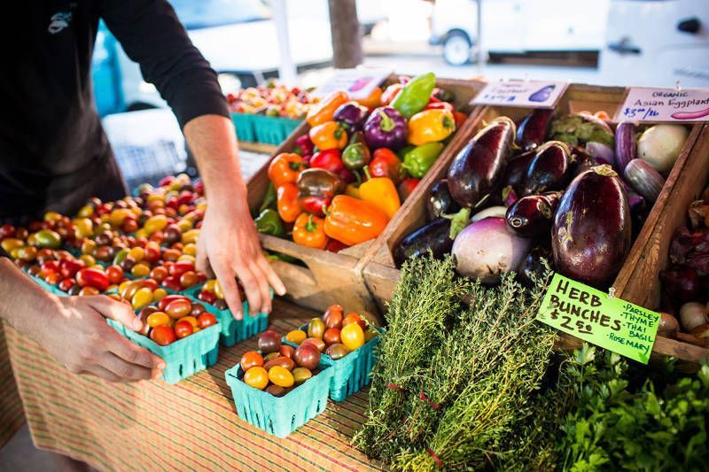 A person is standing in front of a table full of fruits and vegetables.