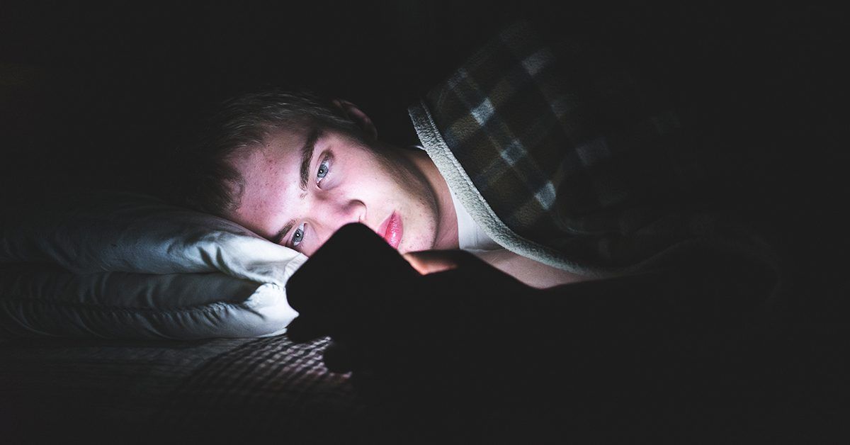 A man is laying in bed looking at his cell phone.