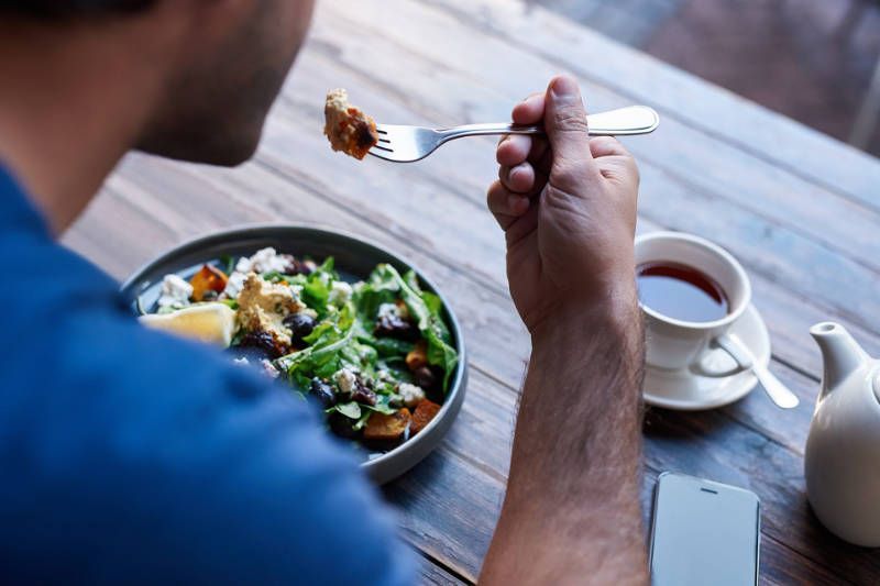 A man is sitting at a table eating a salad with a fork.