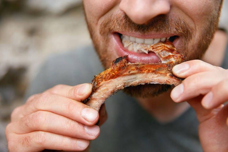 A man is eating a piece of meat with his mouth open.