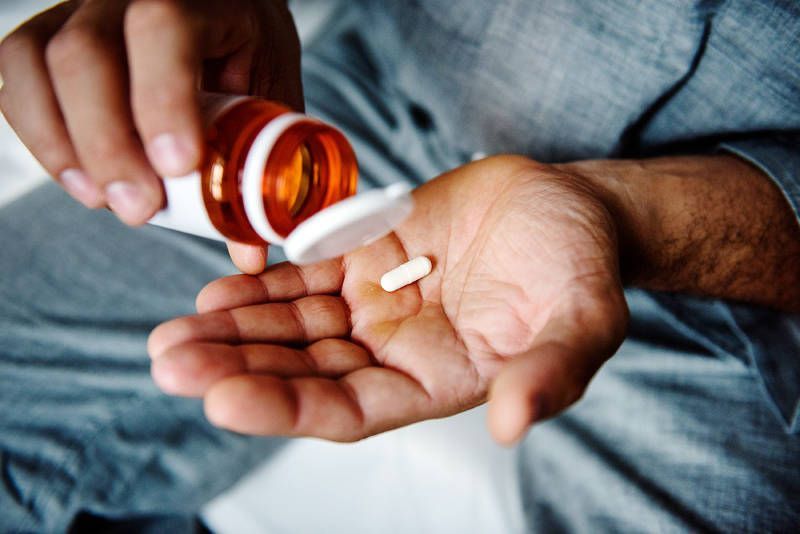 A man is pouring a pill from a bottle into his hand.