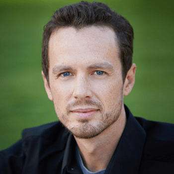 A man with a beard is wearing a black jacket and looking at the camera.