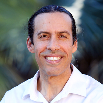 A man with long hair and a white shirt is smiling for the camera.