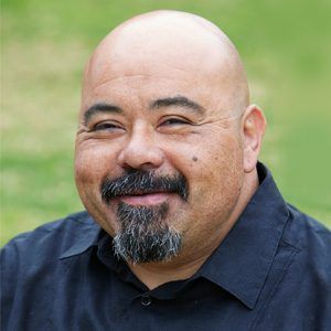 A bald man with a beard is smiling and wearing a black shirt.