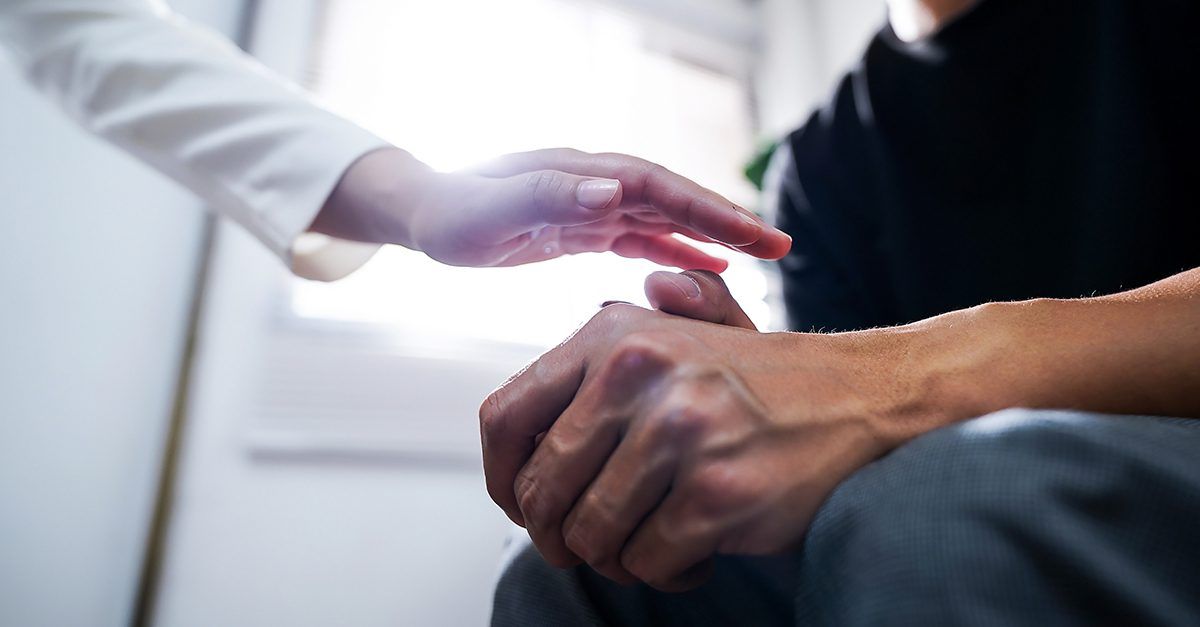 A woman is holding the hand of a man who is sitting down.