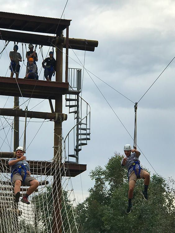 Two people are flying through the air on a ropes course