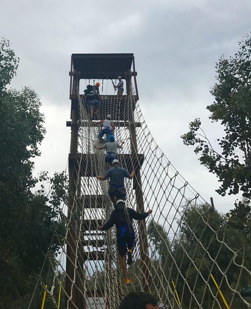 A group of people are climbing up a ropes course