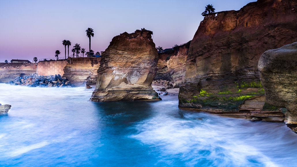 A long exposure photo of a body of water surrounded by rocks and palm trees.