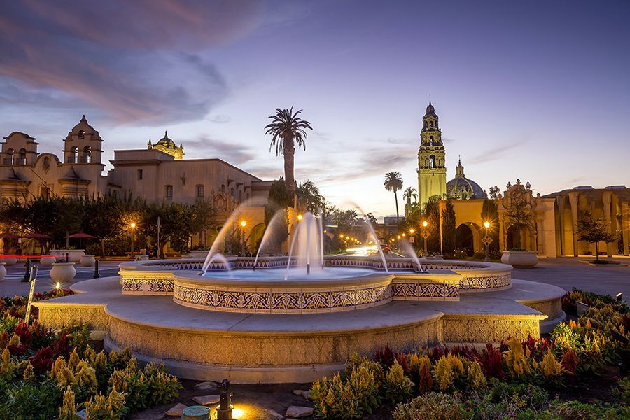 A fountain in a park with a clock tower in the background.
