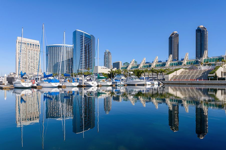 A marina with boats docked and a city skyline reflected in the water.