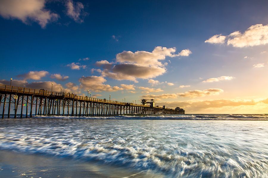 A pier overlooking the ocean at sunset with waves crashing on the beach.