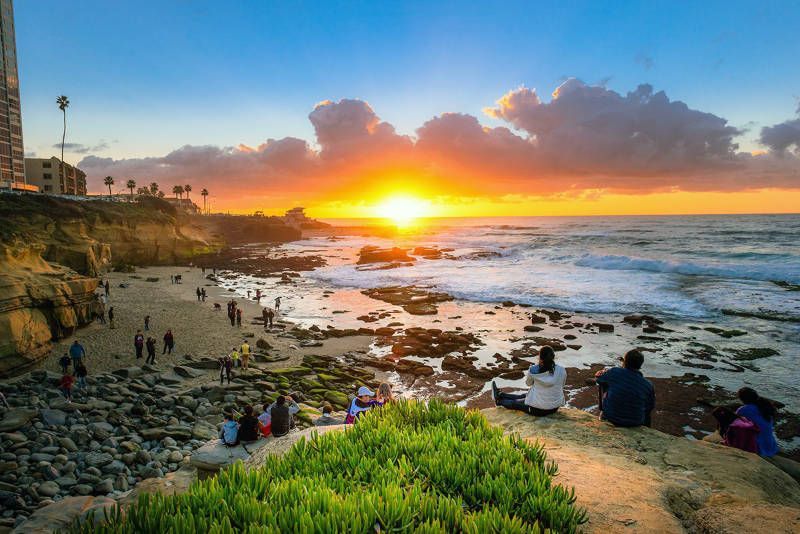 A group of people are sitting on a cliff overlooking the ocean at sunset.