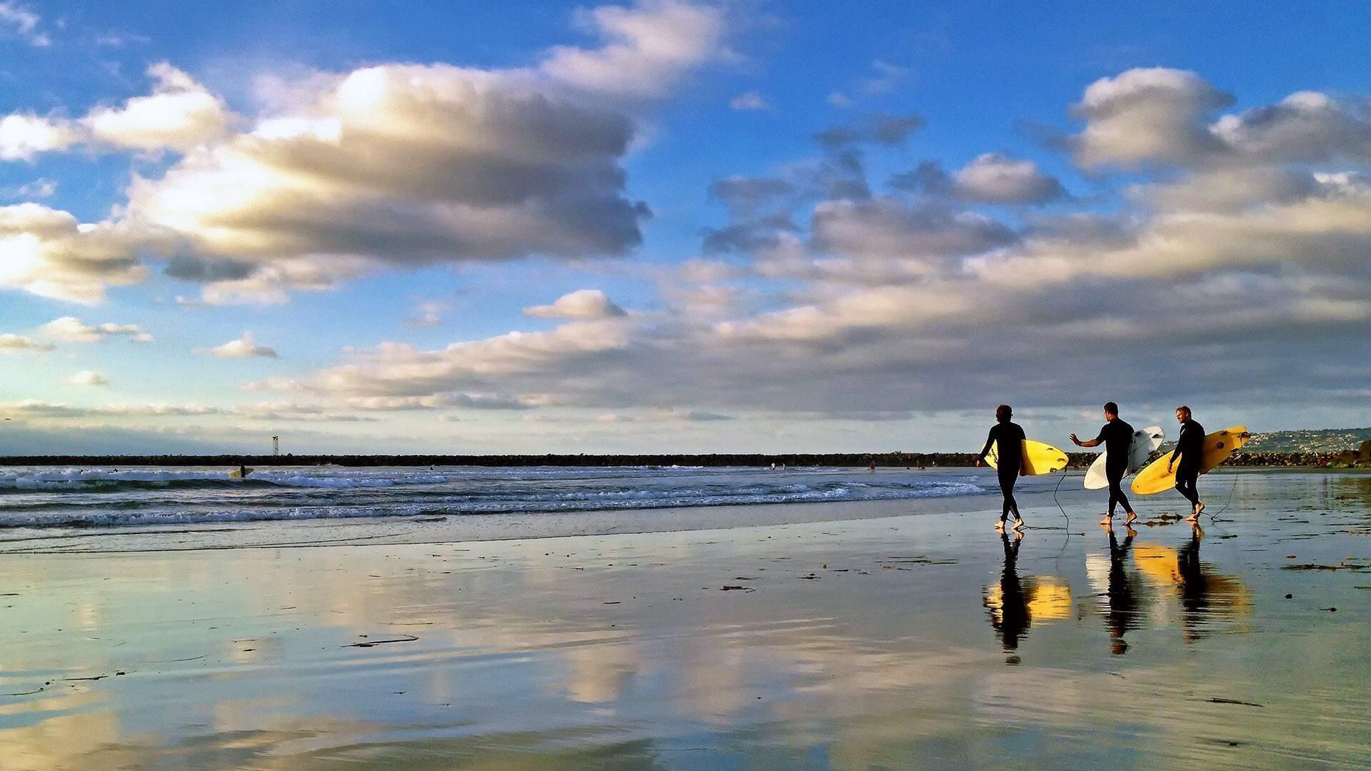 A group of people are walking on a beach carrying surfboards.