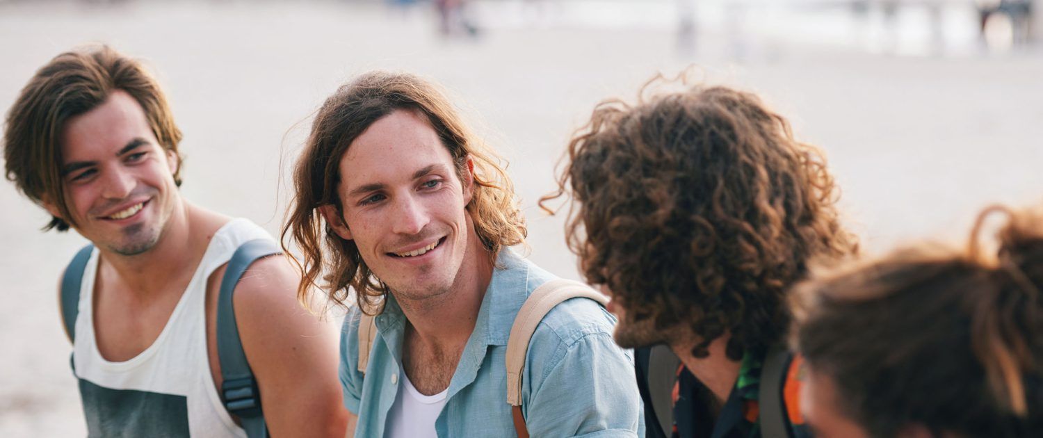 A group of young people are sitting on the beach talking to each other.