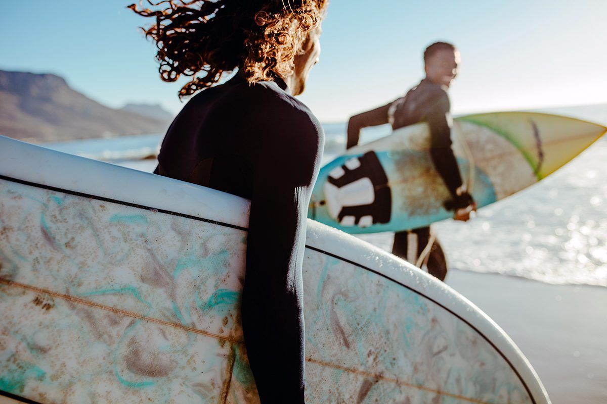 A man and a woman are carrying surfboards on the beach.