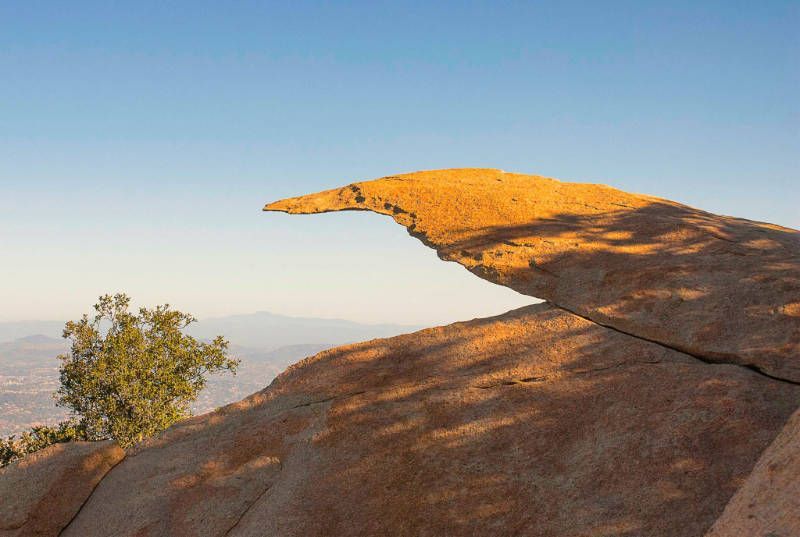 A large rock with a tree in the foreground and a blue sky in the background.