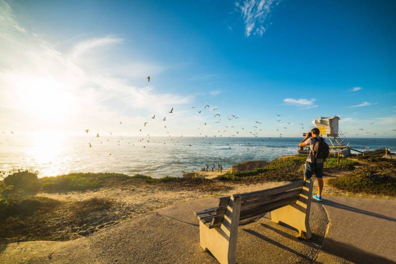 A man is standing on a bench overlooking the ocean.