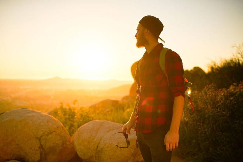 A man with a backpack is standing on top of a hill at sunset.