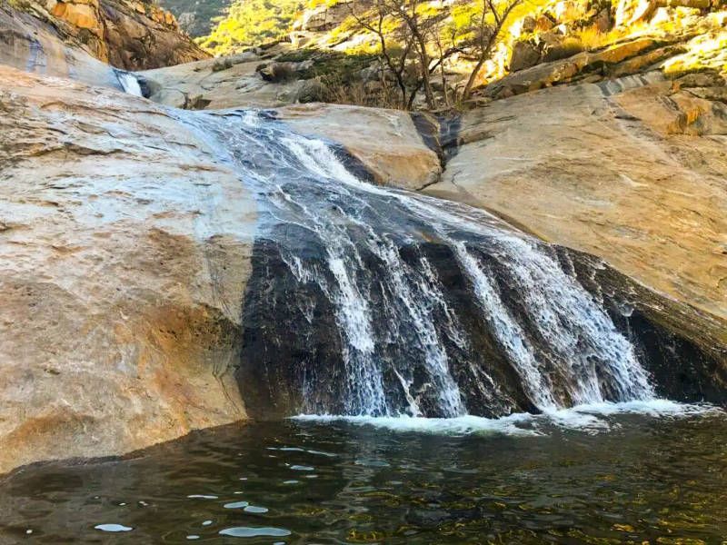 A waterfall is surrounded by rocks and trees and is surrounded by a body of water.