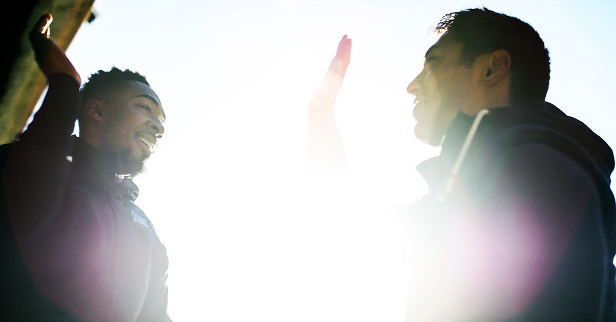 Two men are standing next to each other and giving each other a high five.