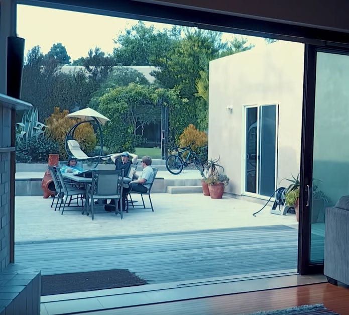 A group of people are sitting at a table outside of a house.