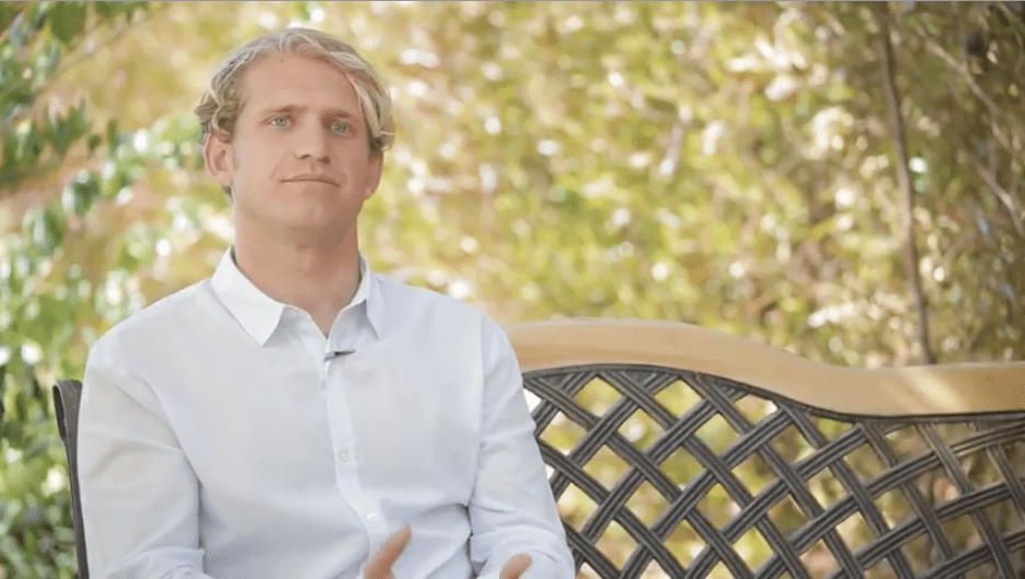 A man in a white shirt is sitting on a bench.