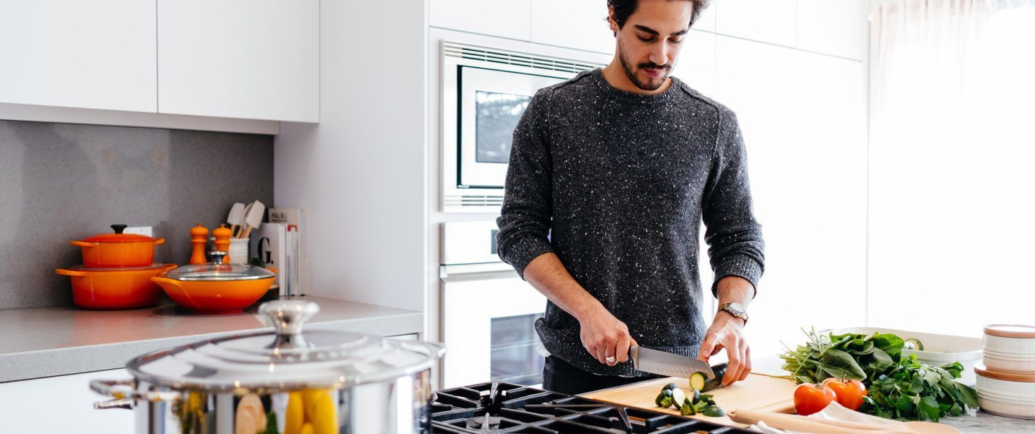 A man is cutting vegetables on a cutting board in a kitchen.