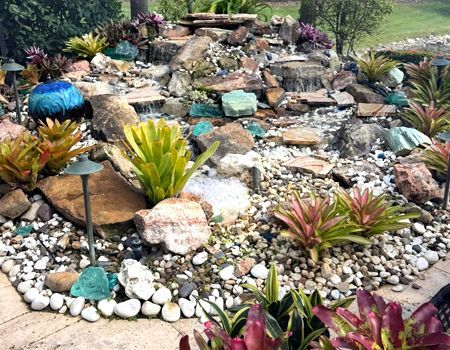 There is a waterfall in the middle of the garden surrounded by rocks and plants.