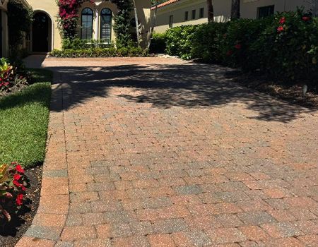 A brick driveway leading to a house with flowers in the foreground.