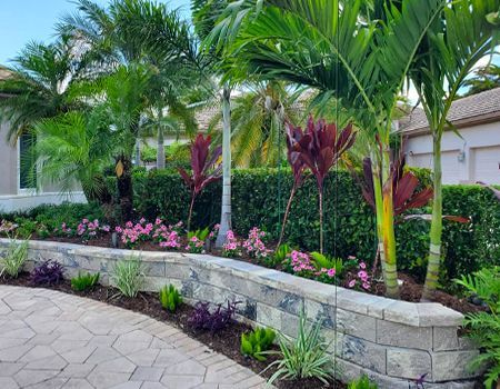 A lush green garden with a brick wall surrounded by palm trees and flowers.