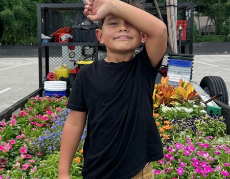 A young boy is standing in front of a trailer full of flowers.