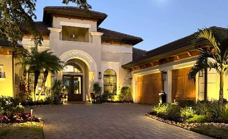 A large house with two garages and a driveway is lit up at night.