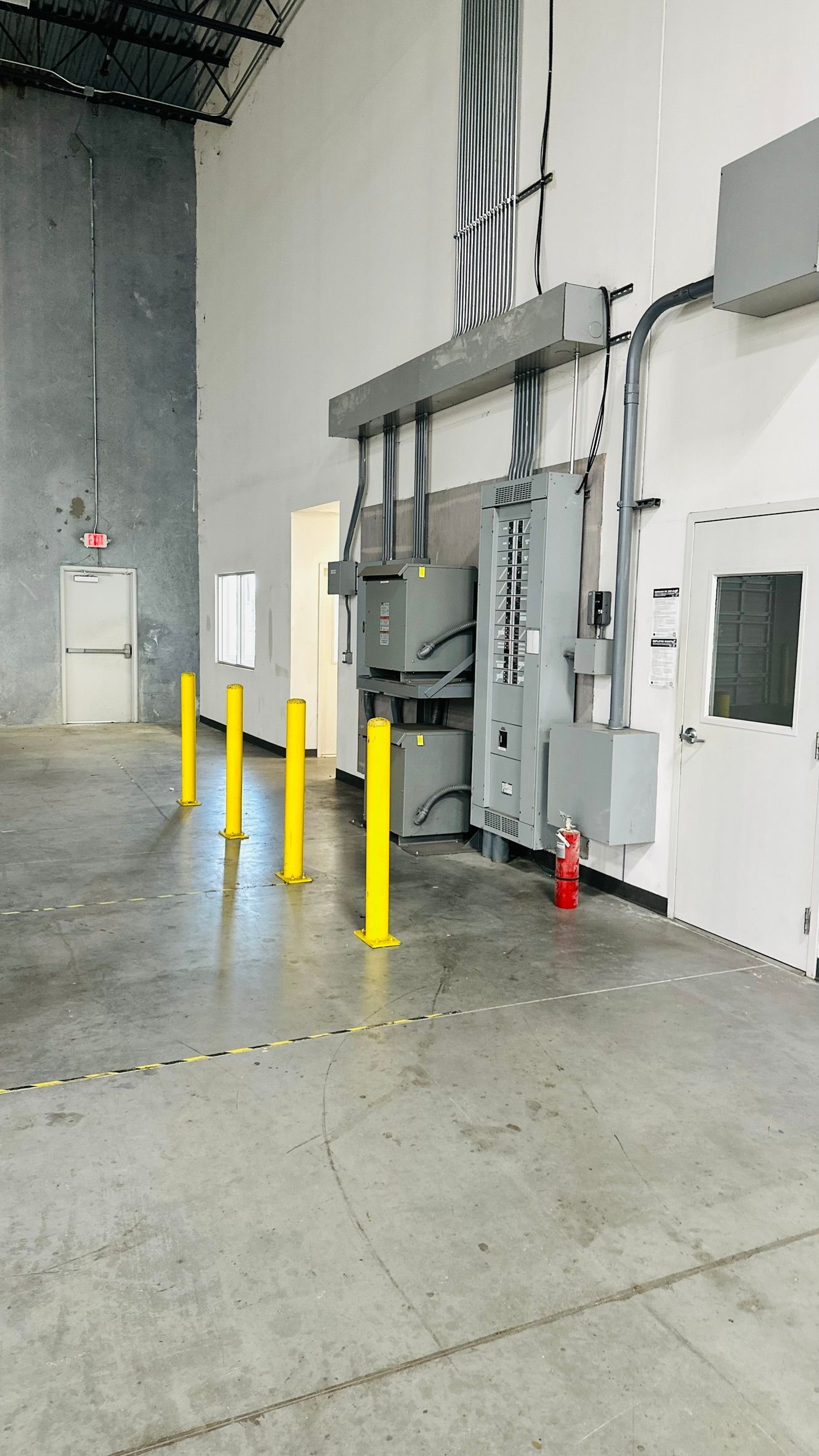 Warehouse interior with electrical panel, fire extinguisher, and yellow bollards.