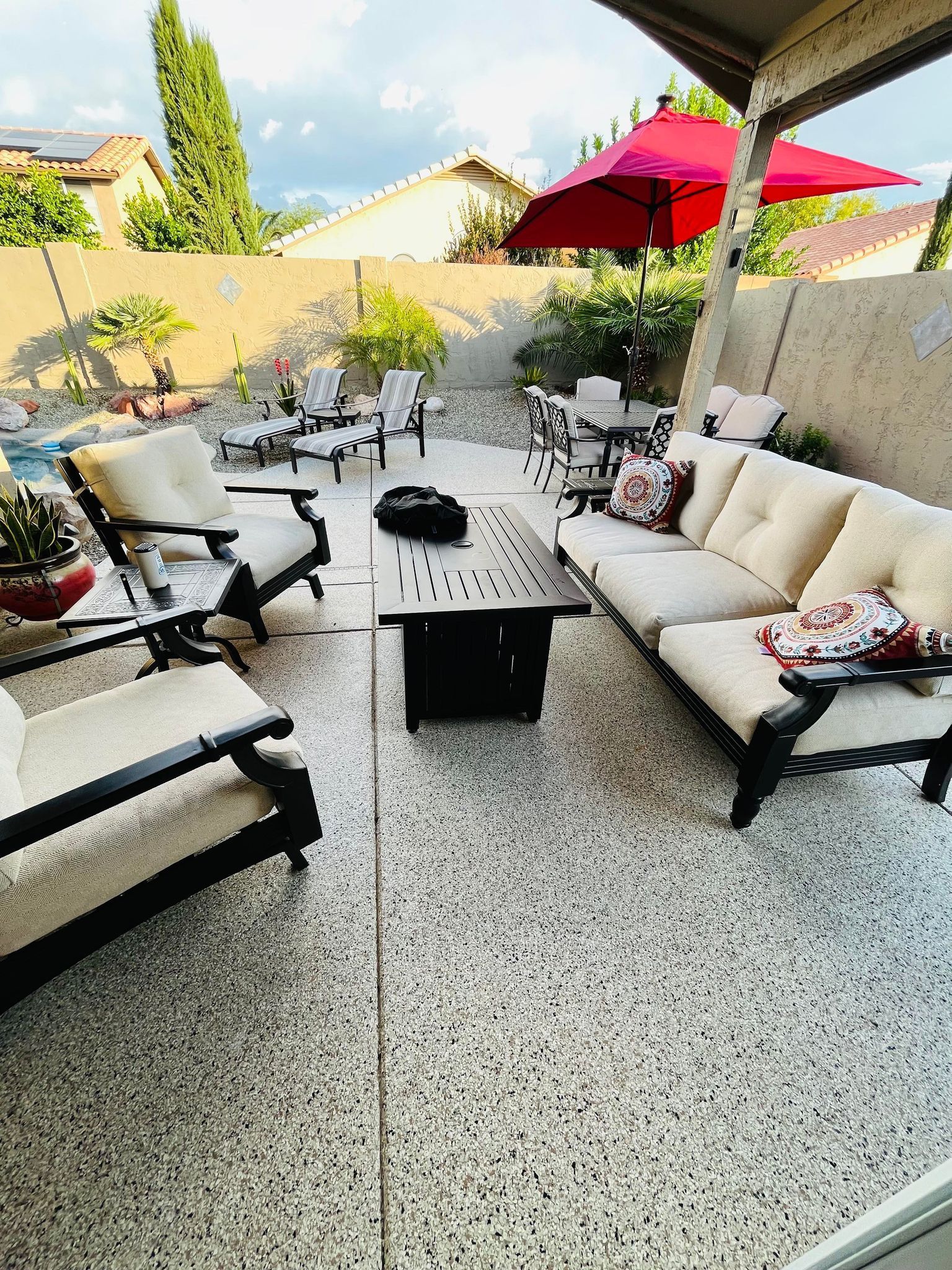 A patio with a couch , chairs , umbrellas and a fire pit.