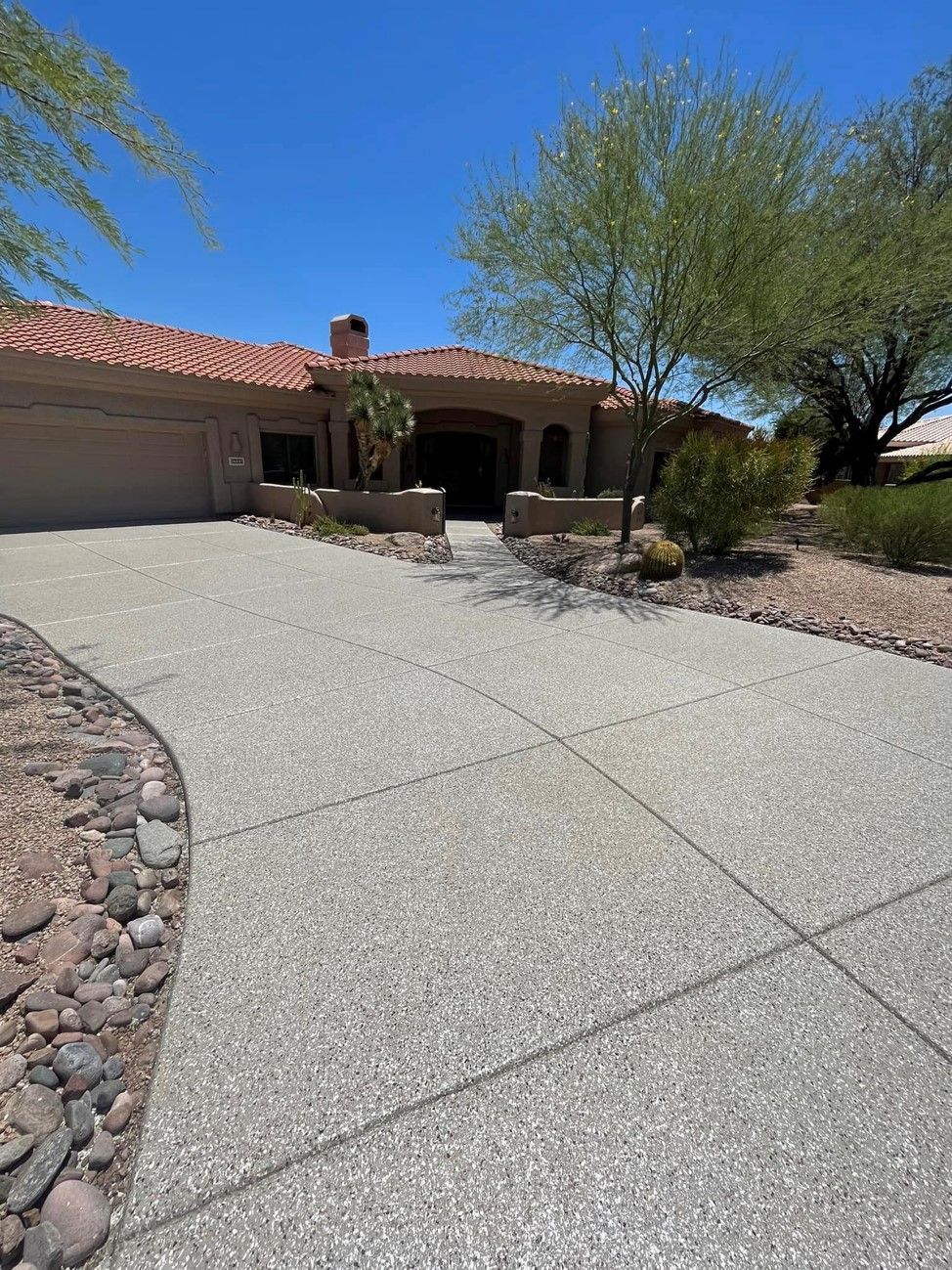 A concrete driveway leading to a large house on a sunny day.