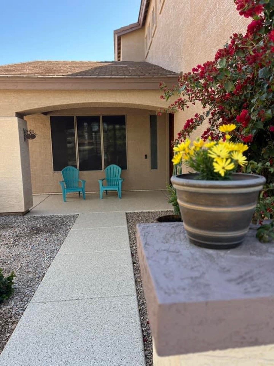 A pot of flowers sits on a sidewalk in front of a house