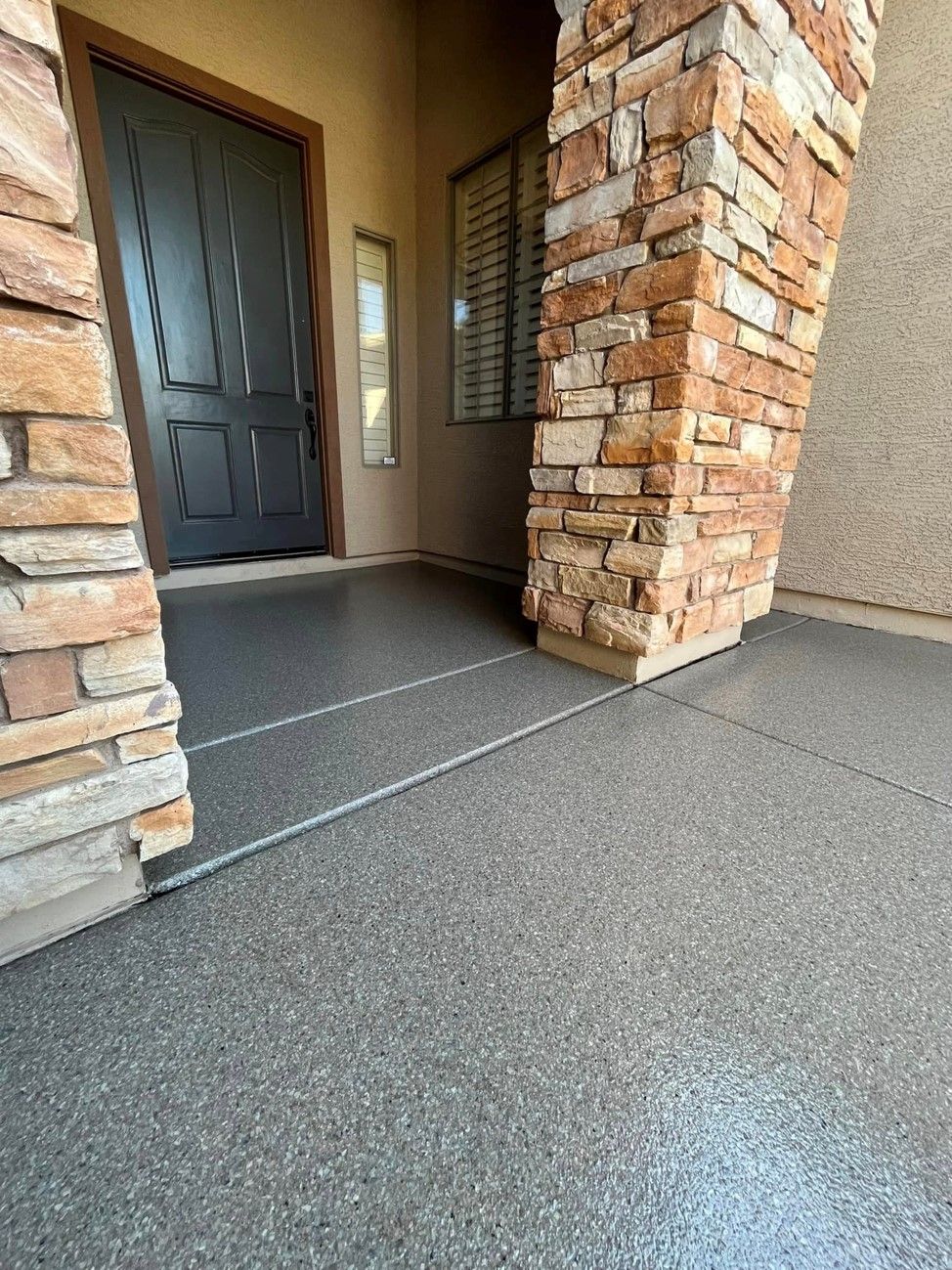A concrete porch with a stone pillar and a black door.