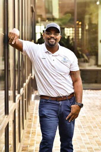 A man in a white shirt and blue jeans is leaning against a wall.