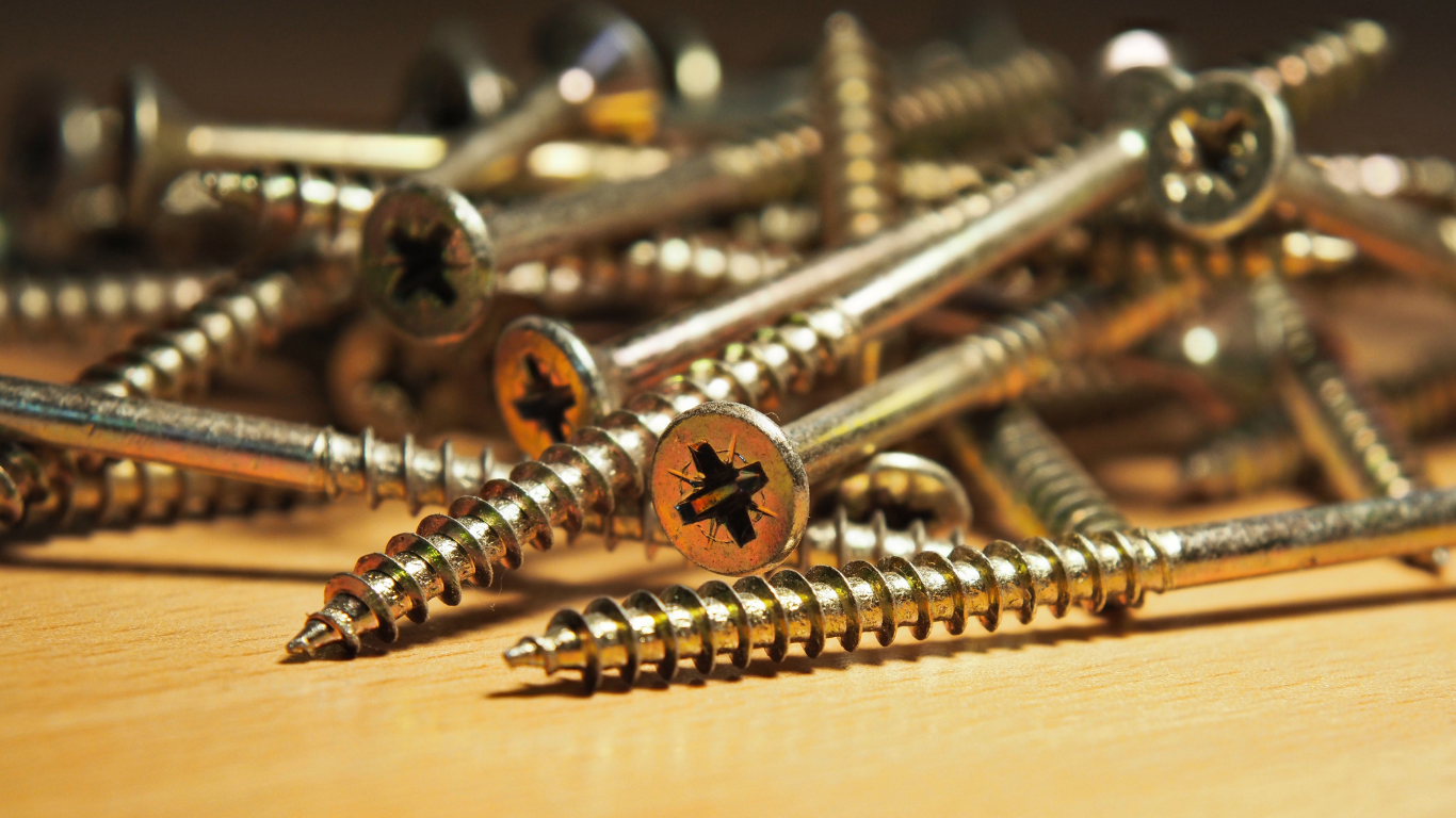 Pile of shiny, golden screws with Phillips head on a wooden surface.
