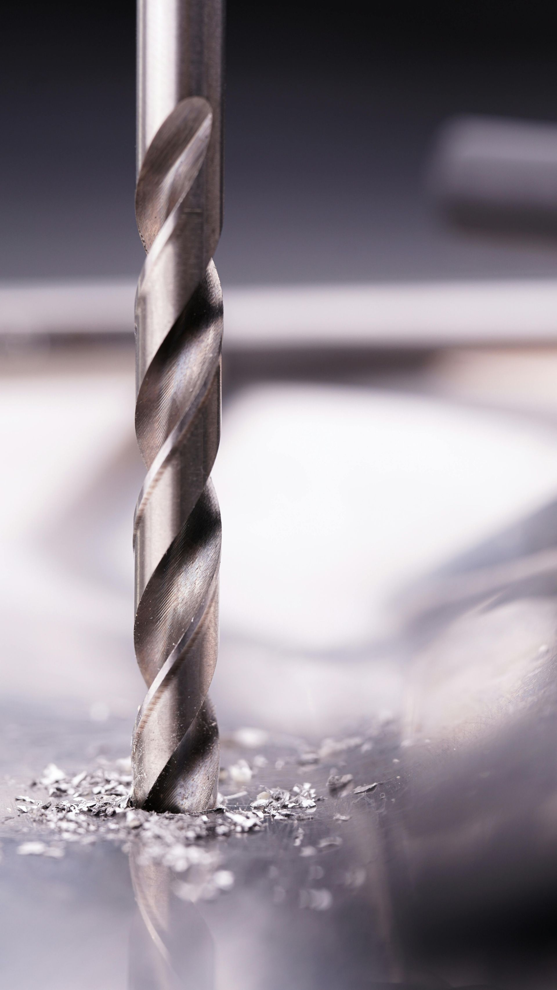 Drill bit creating a hole in a metal surface, producing metal shavings.