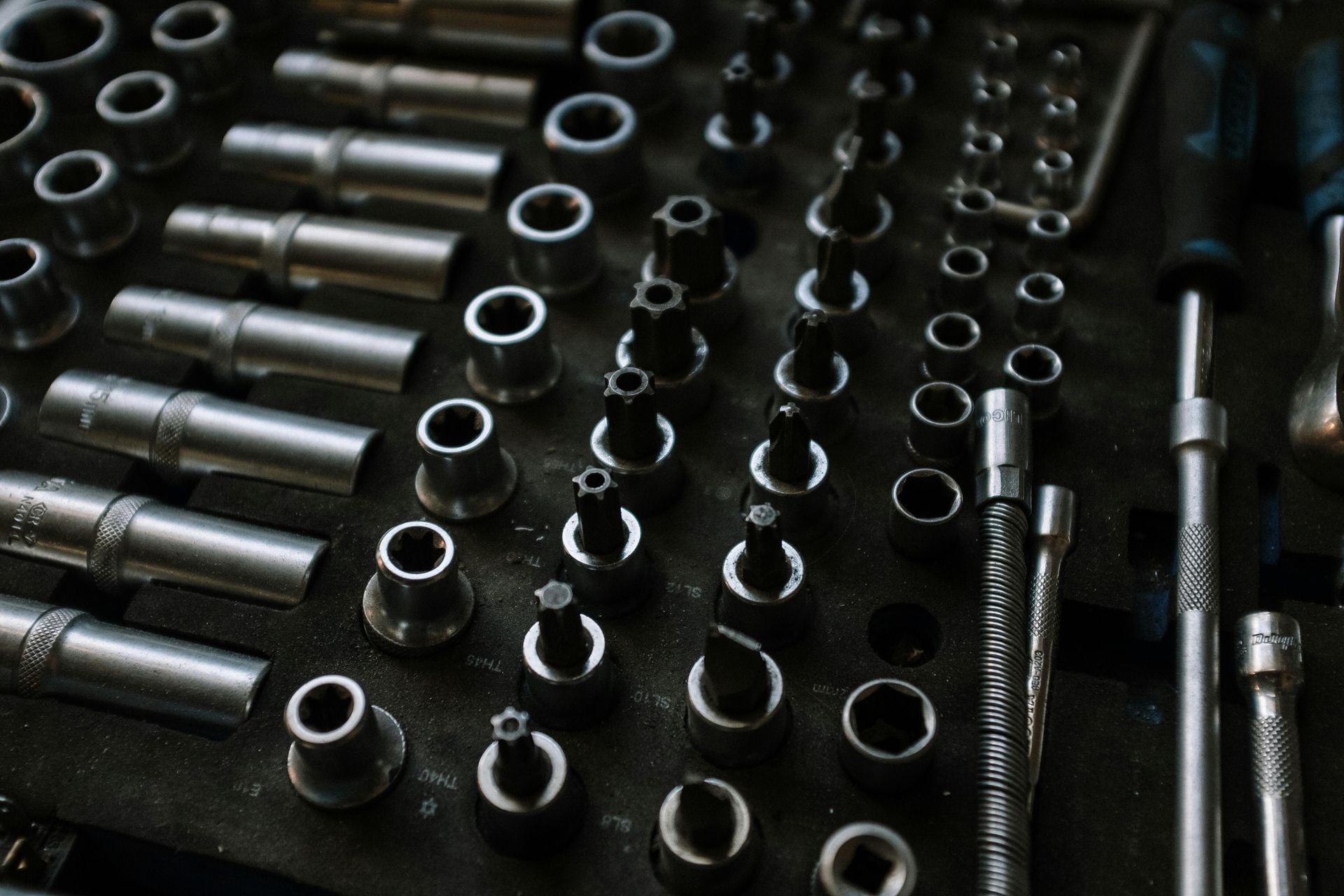 Close-up of a toolbox tray filled with various metal socket wrenches and bits in a workshop setting.
