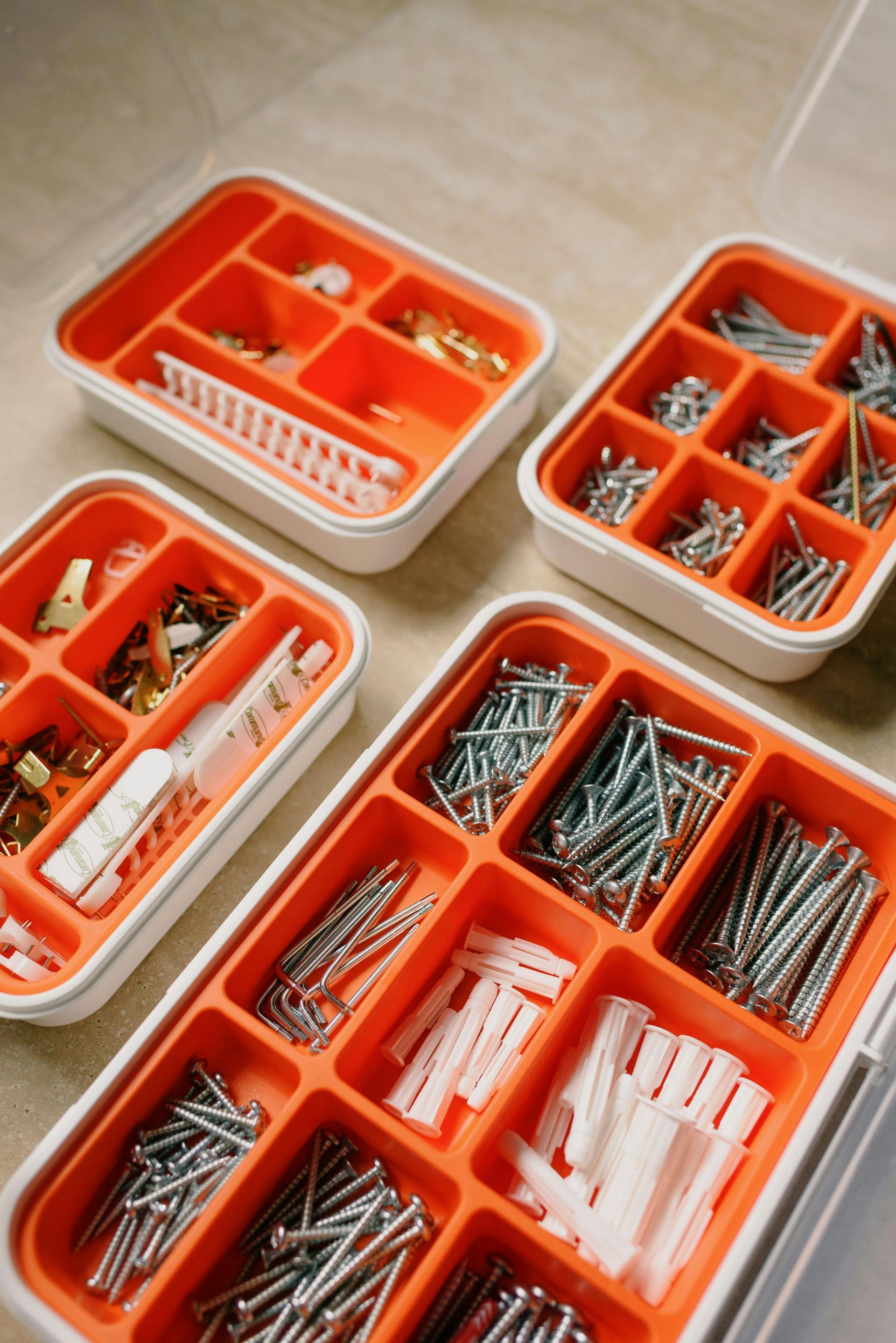 Four orange and white organizer boxes filled with various hardware items on a tiled surface.
