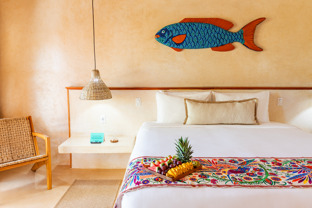 Bedroom with a bed, art, and colorful textiles; a pineapple and fruit sit on the bed.