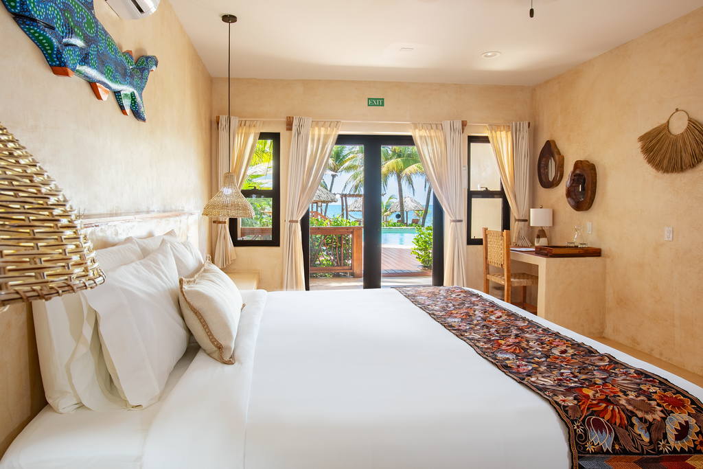 Bedroom with a white bed, open doors to a pool and ocean view, and decorative wall art.