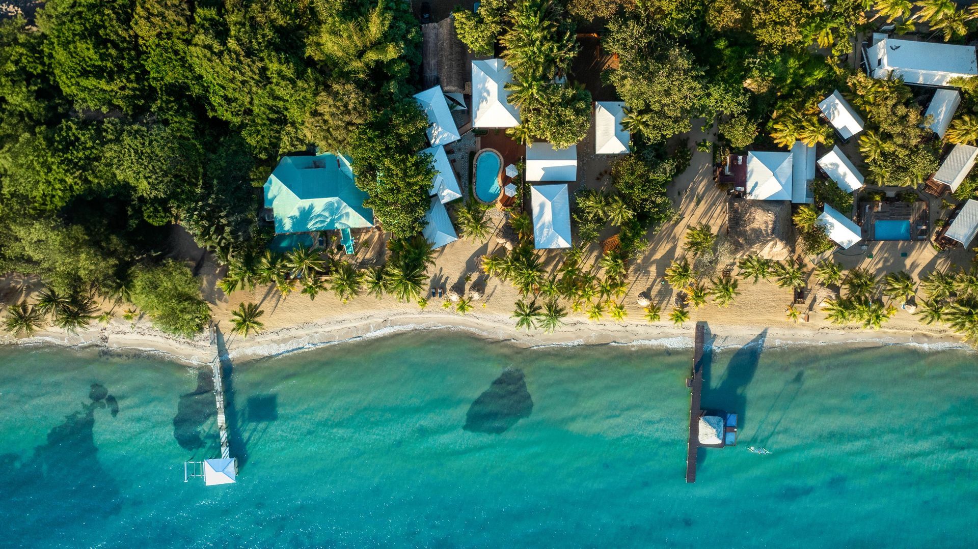 Beachside resort with white buildings, palm trees, and a sandy shore.